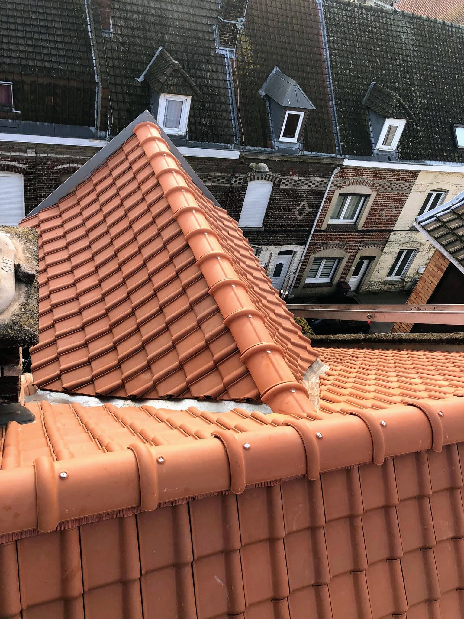 Toiture en panne flamande rénovée, faîtage et rives, devant des façades en brique